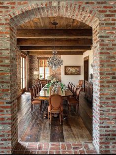 a dining room table surrounded by brick walls and wooden floors with chandelier hanging from the ceiling