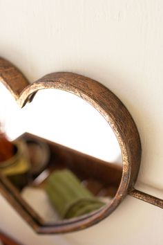 a heart shaped mirror hanging on the side of a white wall next to a wooden shelf