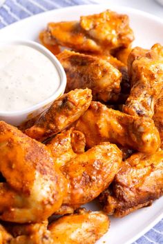 a white plate topped with chicken wings next to a small bowl of ranch dressing on a blue and white table cloth