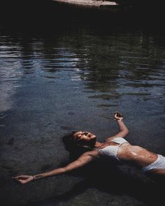 a woman in white swimsuit laying on the water with her hand up to her chest