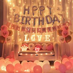 a birthday party with balloons and lights on the wall, couch in front of it