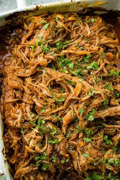 shredded meat in a casserole dish topped with parsley and cilantro