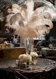 a tall vase filled with white flowers and feathers on top of a black marble table