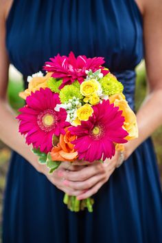 a woman in a blue dress holding a bouquet of colorful flowers on her wedding day