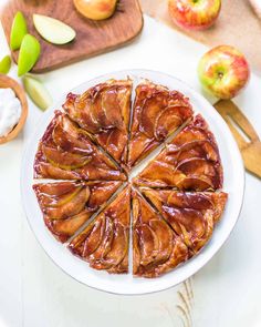 an apple pie is cut into slices on a white plate with apples in the background