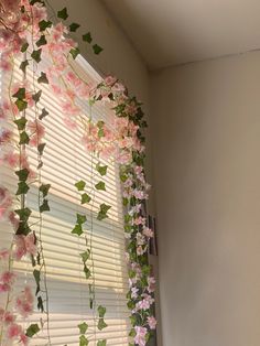 pink flowers hanging from the side of a window sill in front of a blinds