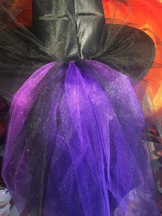 Black satin witch hat with veil and tulle accents in black and purple shades with center jewel. The back of the hat features a cascade of tulle in sparkly shades of black and purple. One size fits up to 22.5 inches head circumference. Various shades of purple are mixed to provide a good color match for most shades of purple. Purple Costume Hats And Headpieces For Halloween, Purple Hats For Halloween Costume Party, Purple Mardi Gras Party Costume Hats And Headpieces, Whimsical Purple Halloween Costume Hats And Headpieces, Purple Halloween Costume Hat, Tulle Witches Hat, Purple Mardi Gras Party Costume Hat, Purple Halloween Party Hat, Purple Witch Headpiece