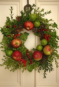 a wreath with apples and greenery hanging on the front door to welcome people into the house