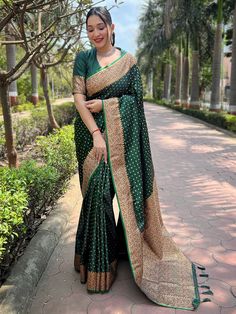 a woman in a green and gold sari standing on the sidewalk with trees behind her