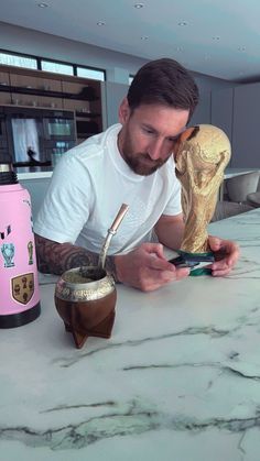 a man sitting at a table next to a cup with a spoon in it and the world cup behind him