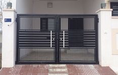 a black gate is open in front of a white building with red bricks on the ground