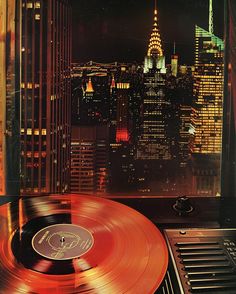 an old record player in front of a window with the city lights lit up at night