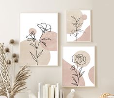 three framed art prints on the wall above a table with books and flowers in vases