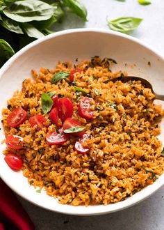 a white bowl filled with rice, tomatoes and spinach on top of a table