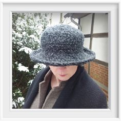 a woman wearing a gray hat and coat in front of snow covered ground with trees