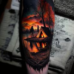 a man's arm with a painting on it that has a campfire and two people