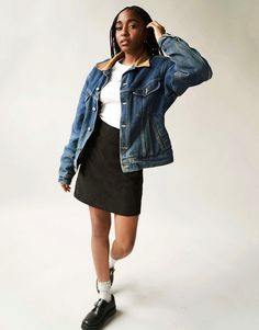 a woman in a denim jacket and skirt poses for the camera with her hands on her head