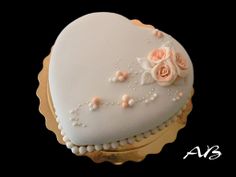 a white heart shaped cake with pink roses on it's side and pearls around the edges