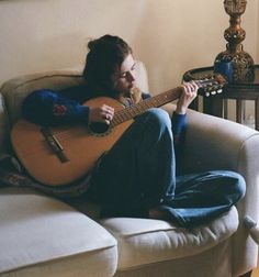 a man sitting on a couch playing an acoustic guitar