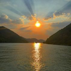 the sun is setting over water with hills in the background and clouds in the sky