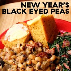 a red plate topped with beans and greens next to a piece of bread on top of a wooden table