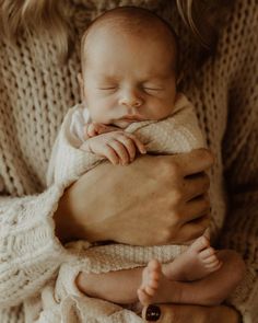 a woman holding a newborn baby wrapped in a white blanket with her hands on her chest