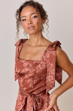 a woman with curly hair wearing a brown floral print dress and holding her hands on her hips