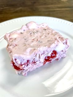 a white plate topped with a piece of cake covered in frosting and cherries