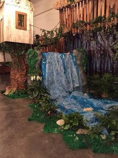 an artificial waterfall in the middle of a room with fake trees and plants around it