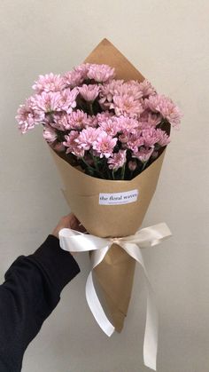 a person holding a bouquet of flowers in their hand with a white ribbon around it