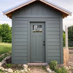 a small gray shed with a wooden roof and window on the front door is shown