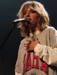 a woman standing in front of a microphone with her hands on her chest and wearing a sweatshirt