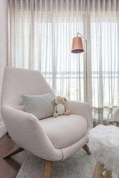 a living room with a chair, lamp and teddy bear on the floor in front of a window