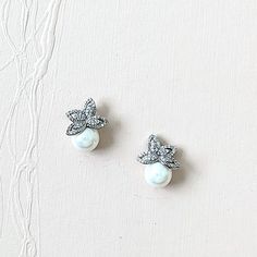 These pearl wedding earrings define muted and understated elegance and class. The solitaire pearls immediately draw the eye in, and the leaf design maintains a level of minimalism that allows the pearls to be the accurate statement here.● Measure about 17mm x 12.5mm.● Cubic Zirconia paves rhodium silver leaf, simulated ivory pearls, nickel-free post.HELP & ADVICEStyling questions or need help finding the right jewelry & accessory or any concern about the design?Please get in touch with me anytim Dainty Silver Bridal Earrings With Pearl Charm, Silver Pearl Earrings For Mother Of The Bride, Silver Classic Pearl Earrings For Mother Of The Bride, Classic Silver Pearl Earrings For Mother Of The Bride, Modern Bridal Earrings, Diamond Earrings Wedding, Simple Bridal Jewelry, Pearl Wedding Earrings, Classic Pearl Earrings