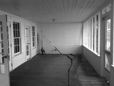 an empty porch with white walls and wood flooring is seen in this black and white photo