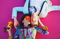 two women laying on the ground with flowers in their hair and one holding her head