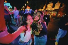 two women standing next to each other in front of a crowd at night with neon lights