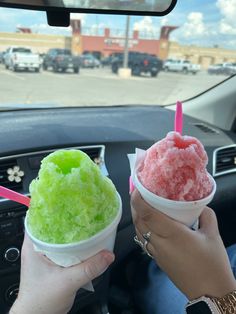 two people are holding up ice cream in their hands while sitting in a car on the street