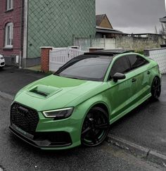 a green car is parked on the side of the road in front of a building