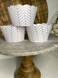 four white paper cups with gold lines on them sitting on a marble stand in front of a wooden wall