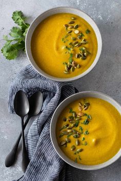 two white bowls filled with carrot soup and topped with pistachio seeds, garnished with parsley