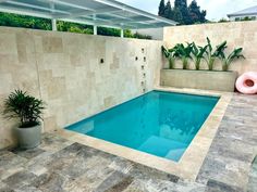 an empty swimming pool in the middle of a tiled floored area with potted plants on either side