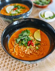 two black bowls filled with soup and garnished with cilantro, lime wedges