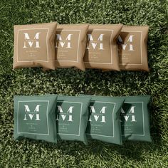 four pillows sitting on top of a green grass covered field next to bags with the letters m and m