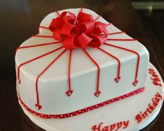 a white cake with red ribbon and bow on top that says happy birthday to you