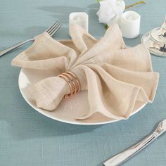 a white plate topped with a napkin and two silver forks next to a vase filled with flowers