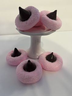 pink donuts with black sprinkles are on a white plate and one is in the middle