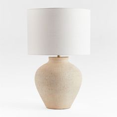 a white table lamp with a beige shade on the base and a light bulb attached to it