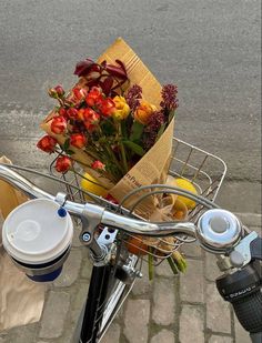 a basket full of flowers sitting on the back of a bike with a cup of coffee