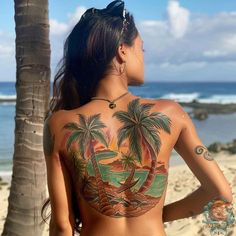 a woman with tattoos on her back standing in front of the ocean and palm trees